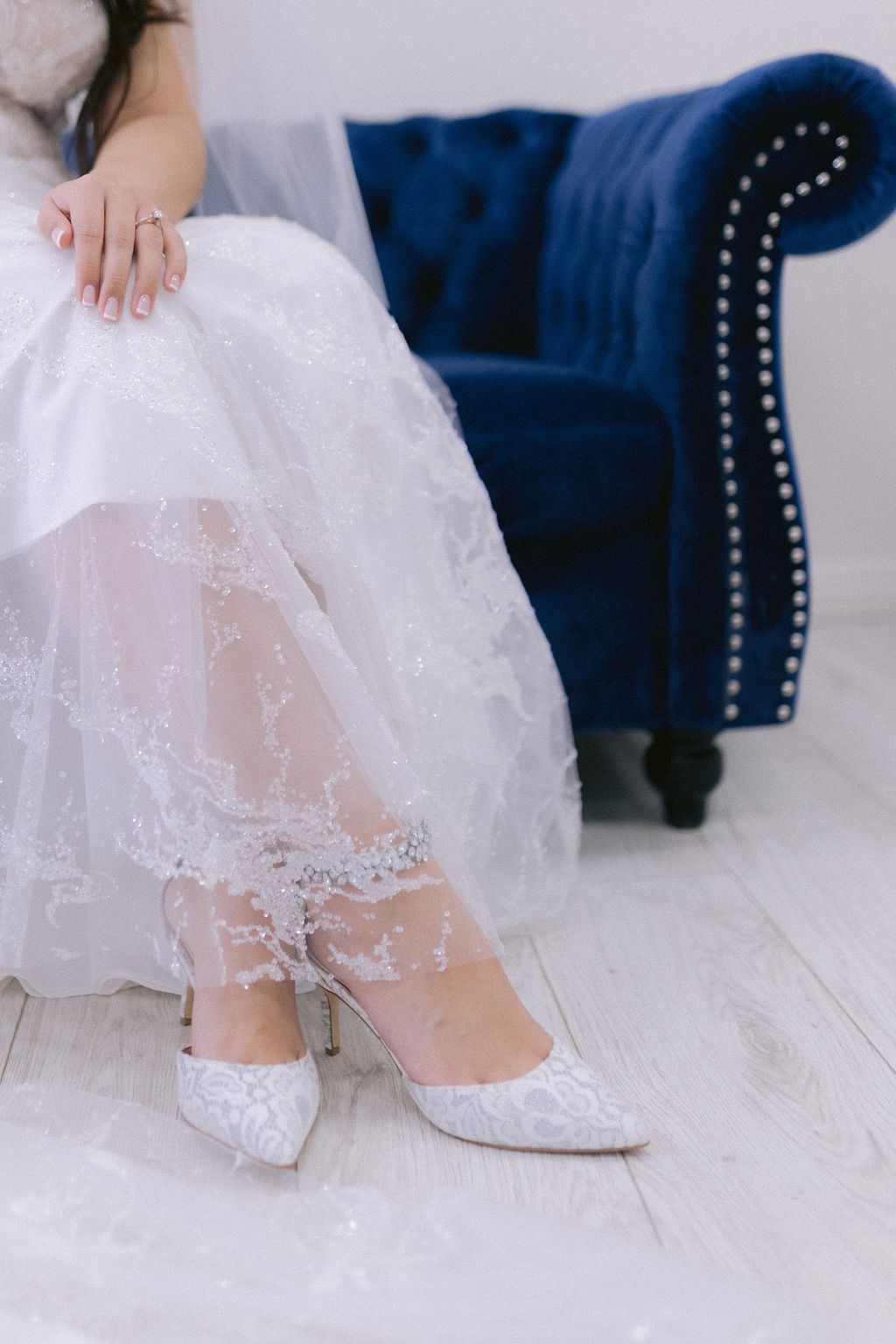 Close up of the brides wedding dress cascading across her lace white heels. 