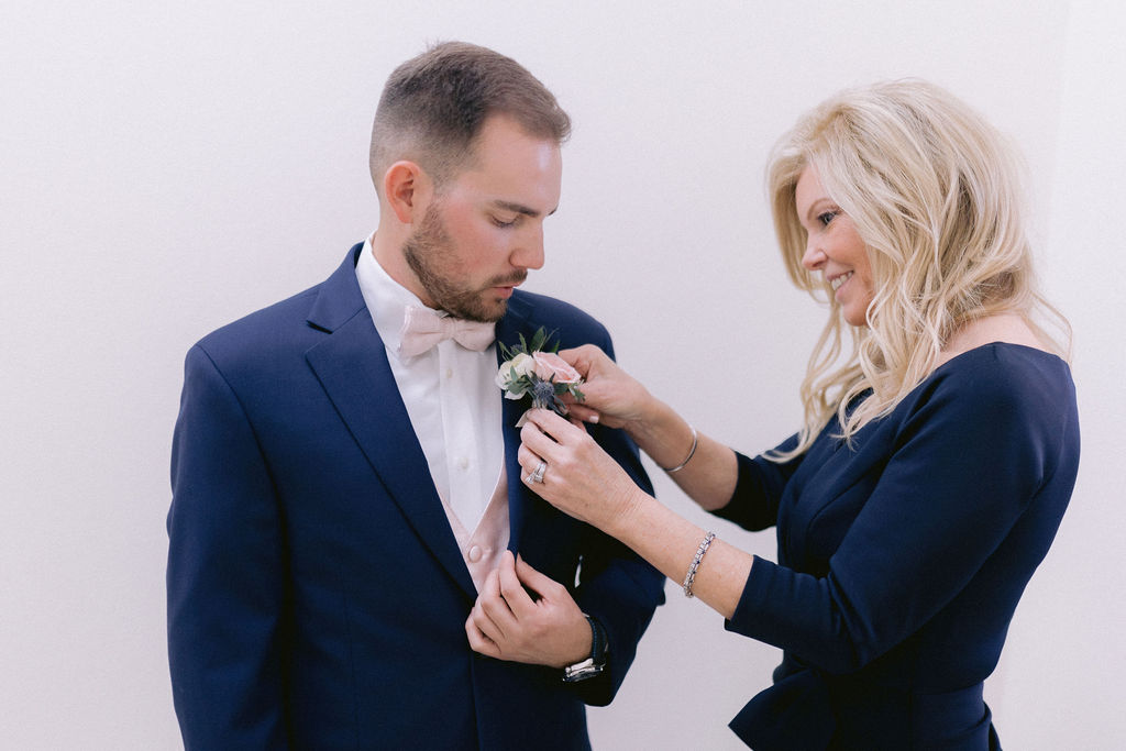 Groom getting his boutonniere placed by her mother.  
