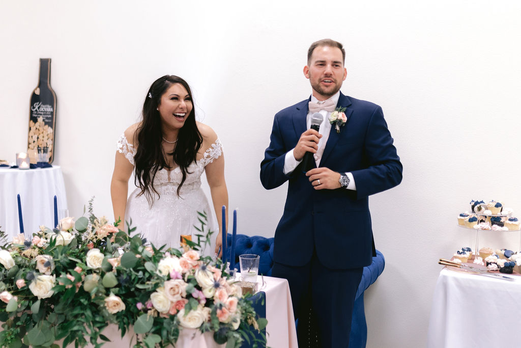 Navy Blue & Blush Pink Micro-Wedding bride laughs as the groom gives a speech from their sweetheart table. 