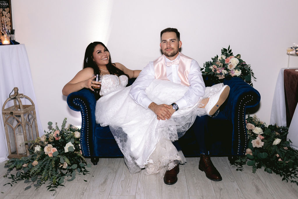 Bride and groom relaxing after dancing with guests on a comfy couch. The bride changing into comfy white tennis shoes. 