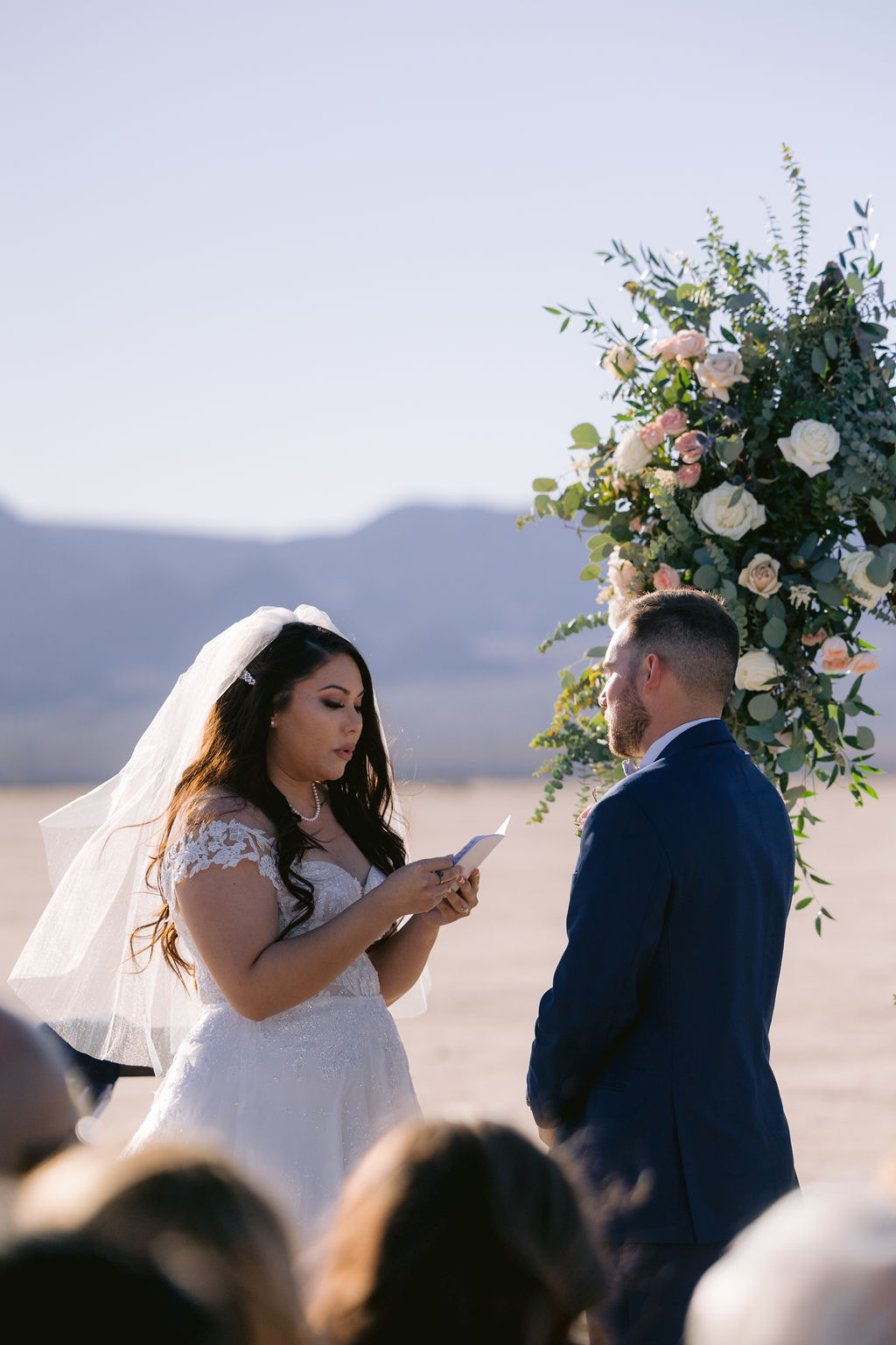 Navy Blue & Blush Pink Micro-Wedding Bride reads her vows to the groom. Her beautiful floral arch in the background. 