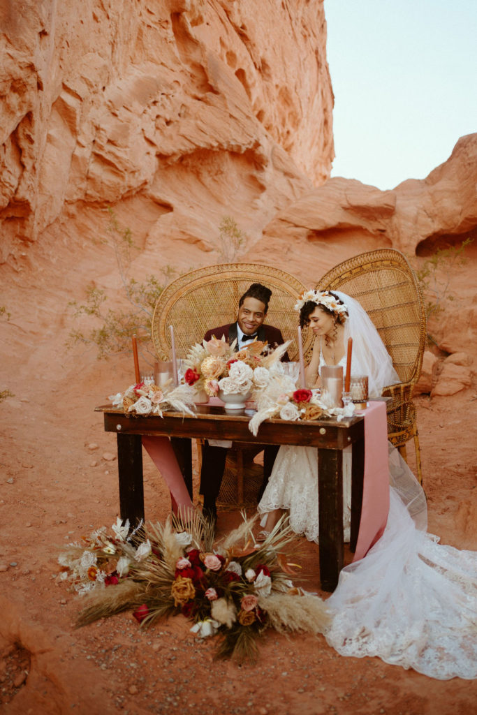 Romantic Mauve & Desert Hues Elopement bride and groom sitting at their sweetheart table with gorgeous woven chairs. 
