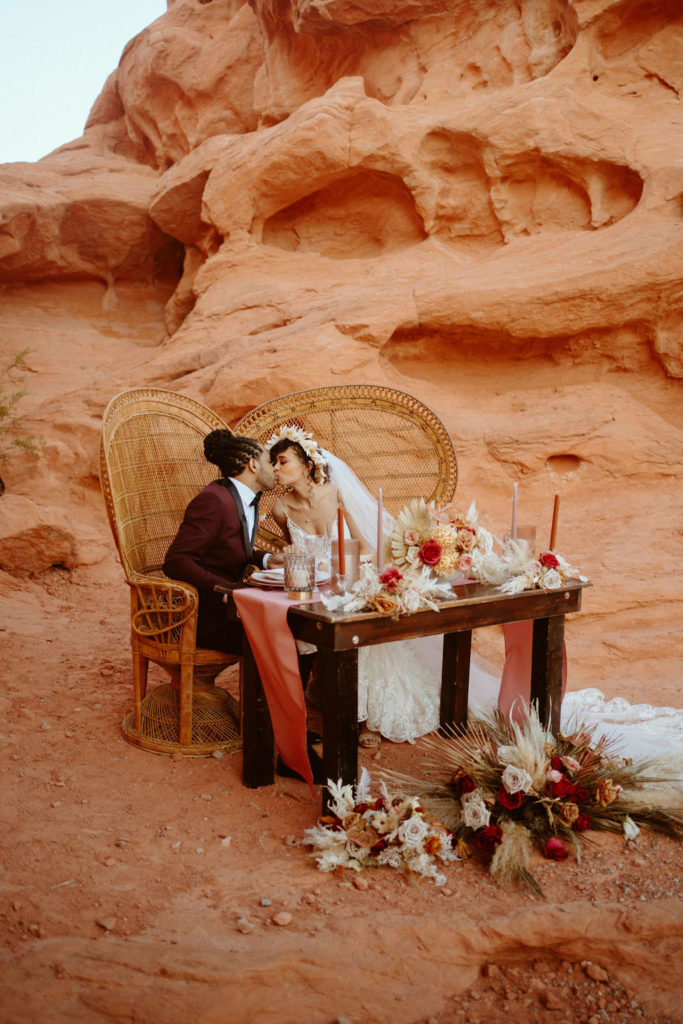Bride and groom sharing a kiss at their sweetheart table in the desert. 