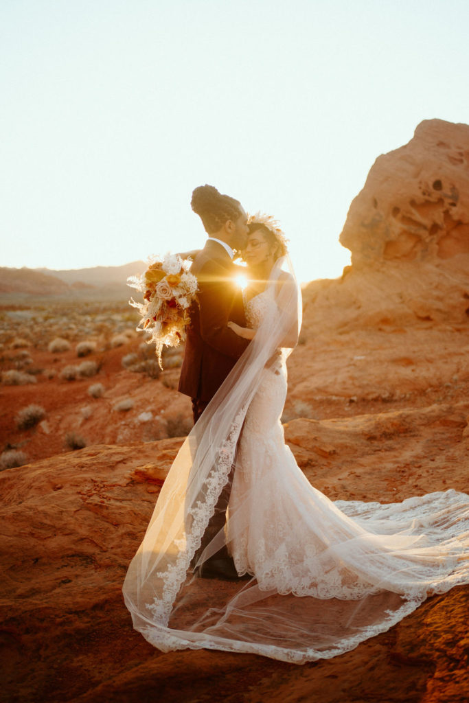 Desert sunset peaking through the bride and groom embracing. 
