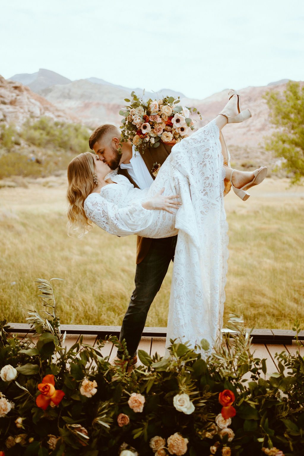 The groom holds the bride in a craddling position as he dips her into a kiss. Her feet kicking out into the air as her white lace train flows down to the ground. 