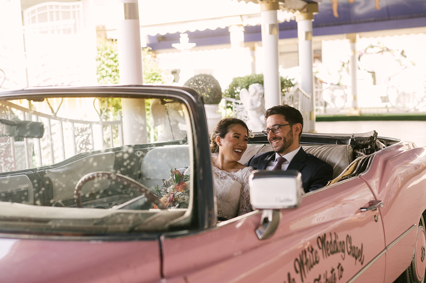 Newlyweds sitting in the world famous pink Cadillac smiling and laughing 