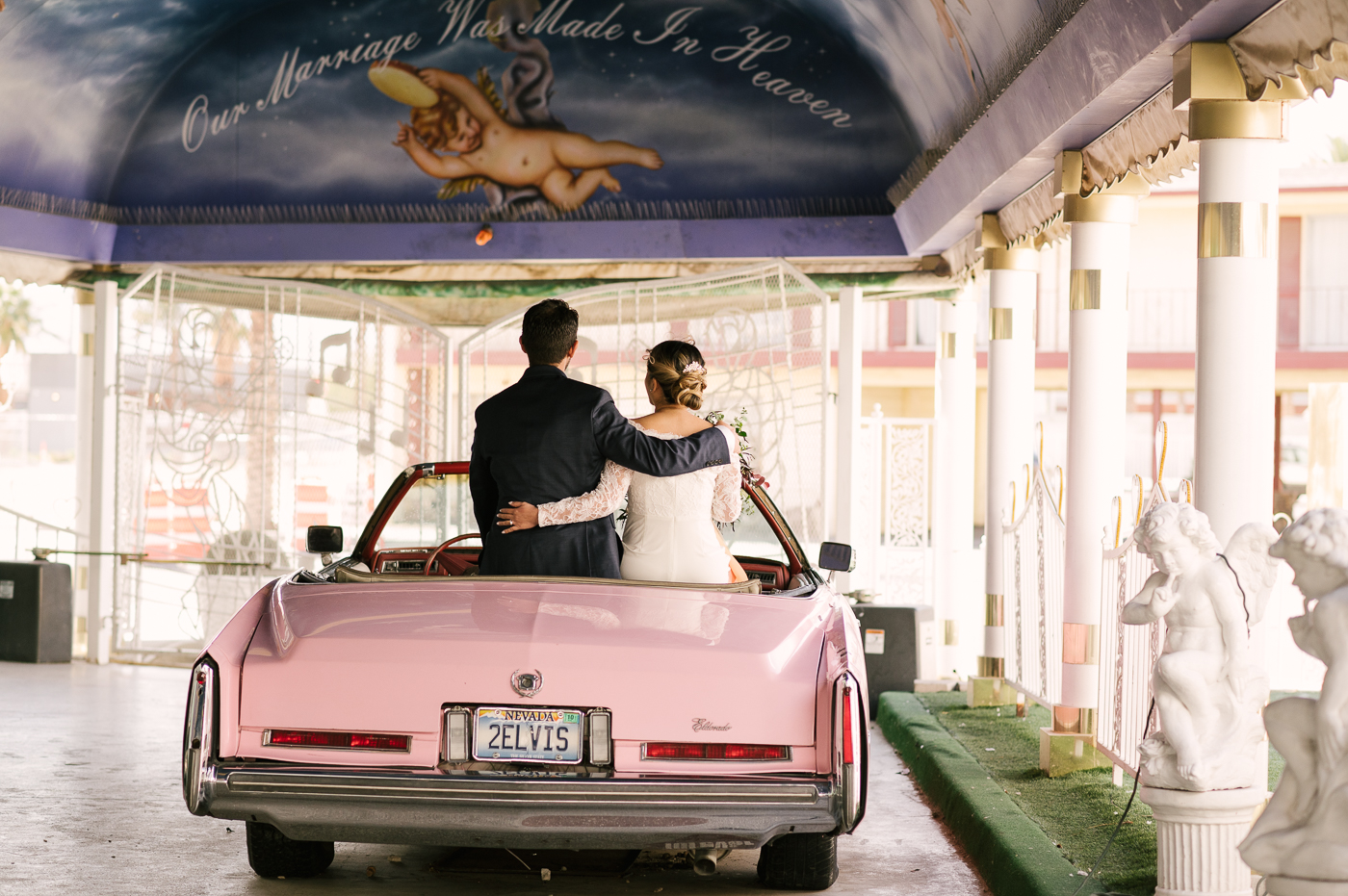 Bride and Groom sitting on the trunk of the world famous pink Cadillac holding each other. 