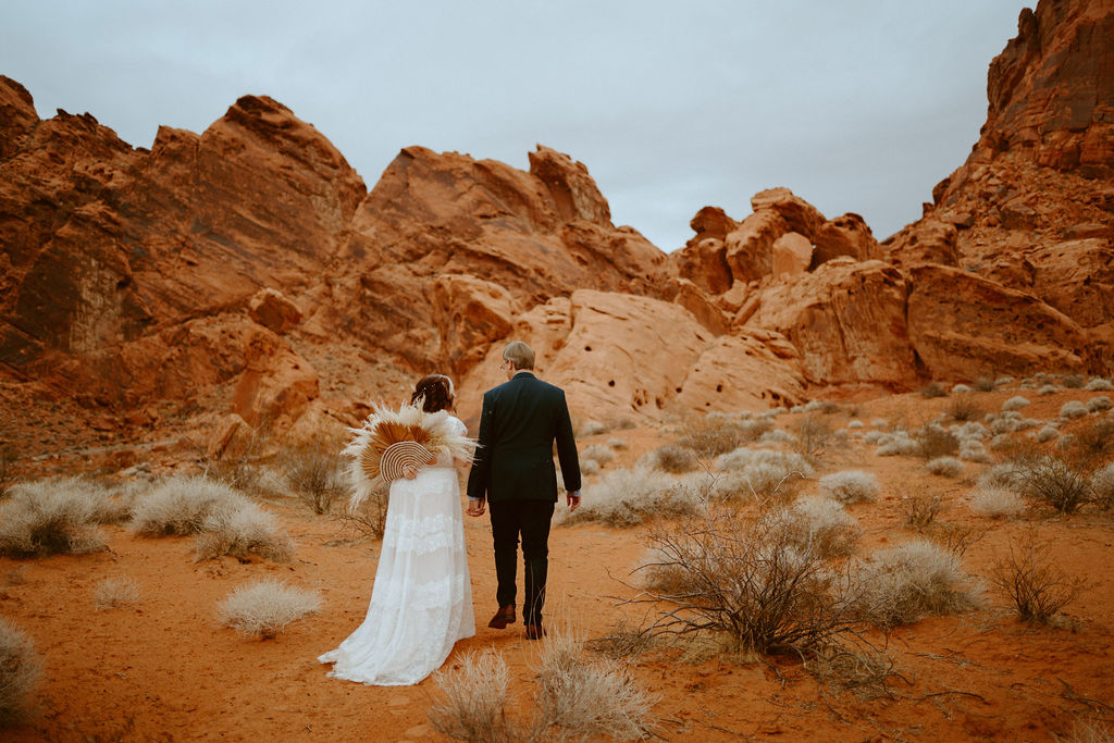 Bride holding pampas grass bouquet behind her back while walking with groom in Visitor Center Valley of Fire Elopement