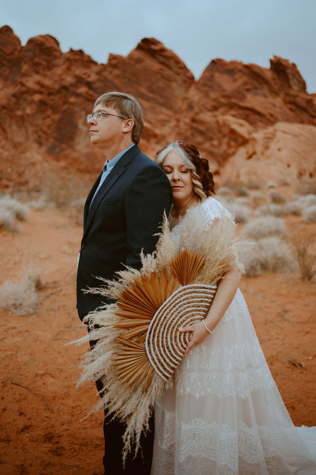 Bride holding pampas grass bouquet rests on grooms back while he looks off into the distance at Valley of Fire State Park 