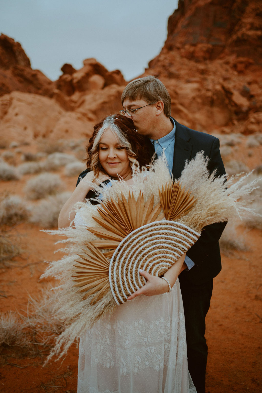 Bride holding pampas grass bouquet while groom kisses her during their Las Vegas desert destination wedding 