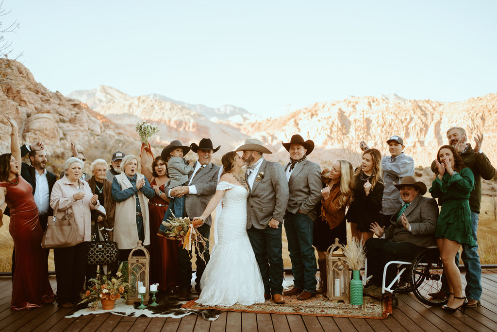 Family and Friends Cheering while Newlyweds Kiss and Red Rock Canyon in the background for Western Inspired Turquoise Boho Elopement 
