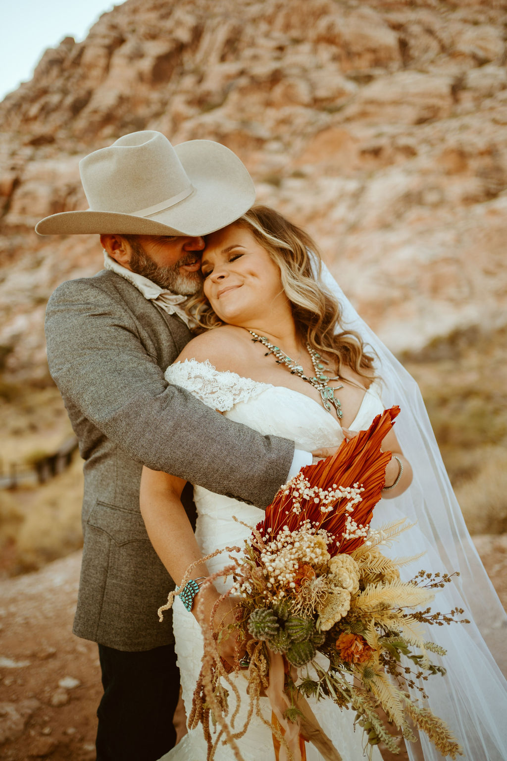Bride with Turquoise Jewelry and western boho bouquet being hugged by groom after ceremony 