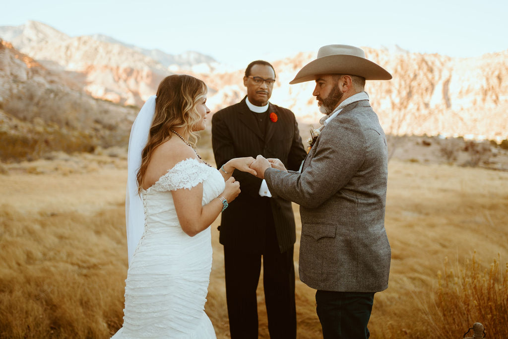 Groom putting ring on Brides Finger with Red Rock Canyon in Background for Western Inspired Turquoise Boho Elopement 