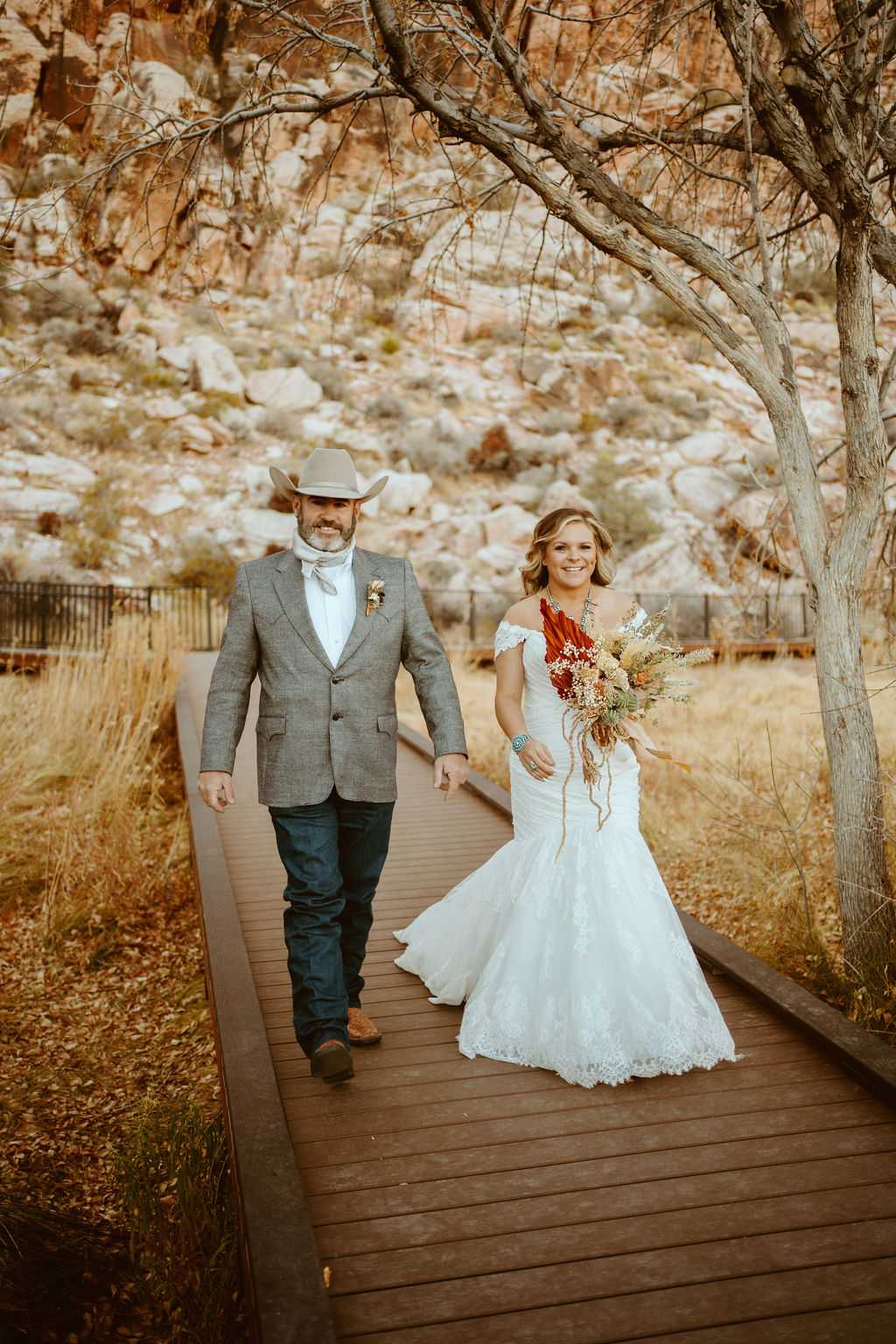 Bride in Mermaid Wedding Dress and Dried Floral Bouquet walking with Groom in Red Rock Canyon 