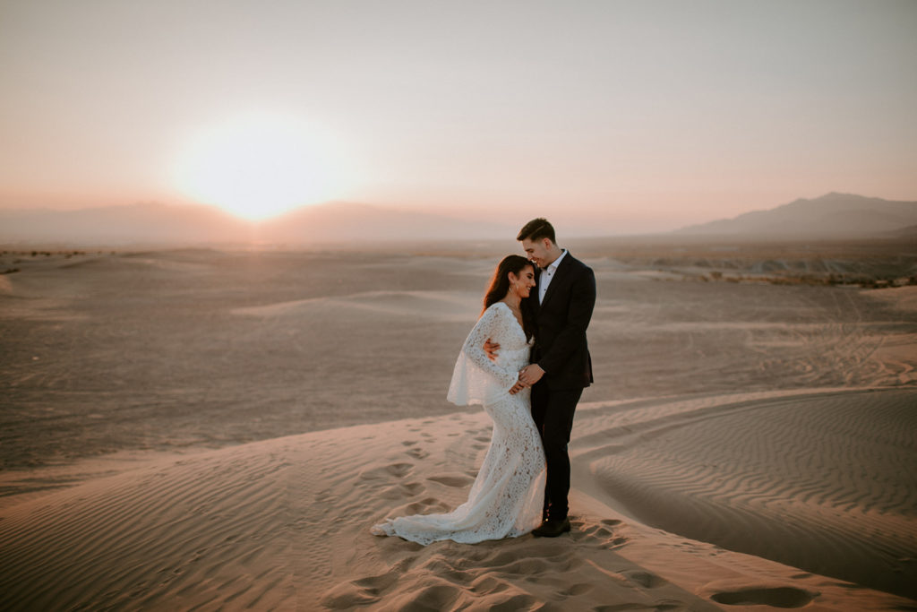 How To Start Planning a Destination Wedding. Couple standing in the middle of the dunes of the revere golf club located in Las Vegas with a beautiful sunset setting behind them.