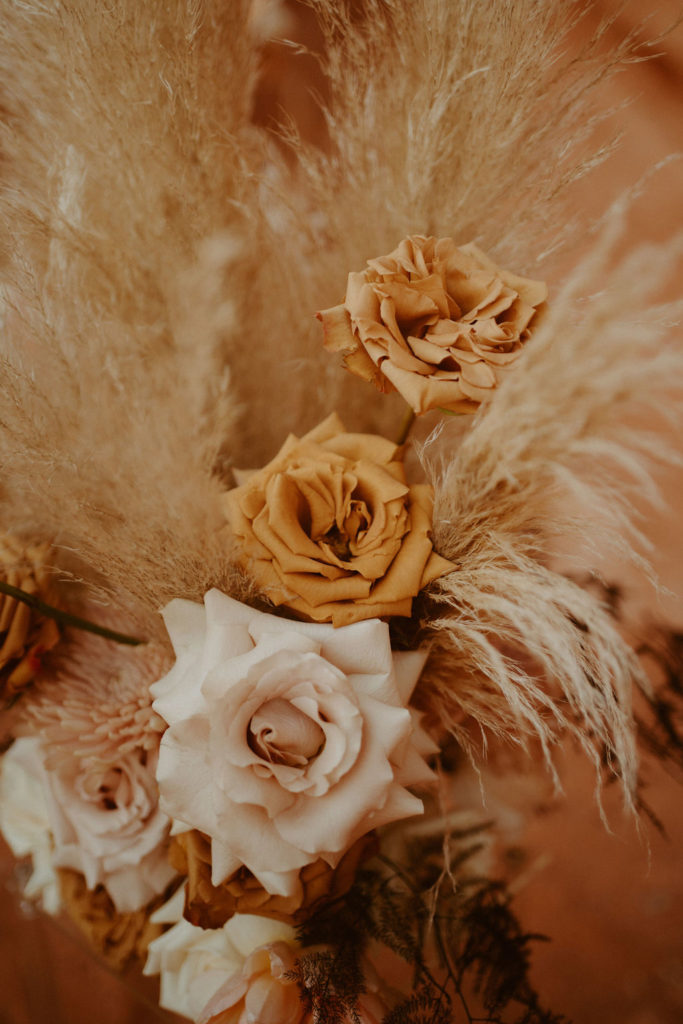 Close up shot of cream and toffee colored roses surrounded by pampas. 