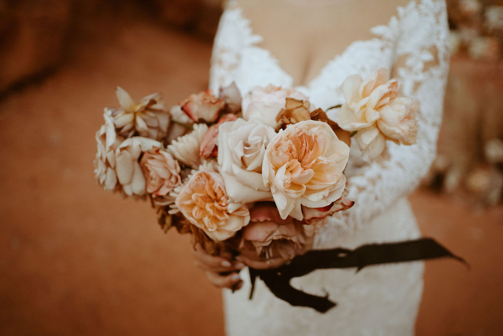 Close up of the brides peach, cream, soft pink, and toffee colored bridal bouquet. With long black frayed ribbon. 
