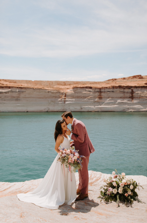 Couple standing on red rocks in Lake Powell Arizona, overlooking the turquoise blue water of the natural man-made lake, Celebrating their vows as a newlywed couple