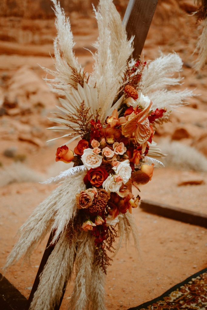 What is a boho styled wedding. Boho style floral arrangement mixed with deep colored roses and dried florals on triangle arch at valley of fire