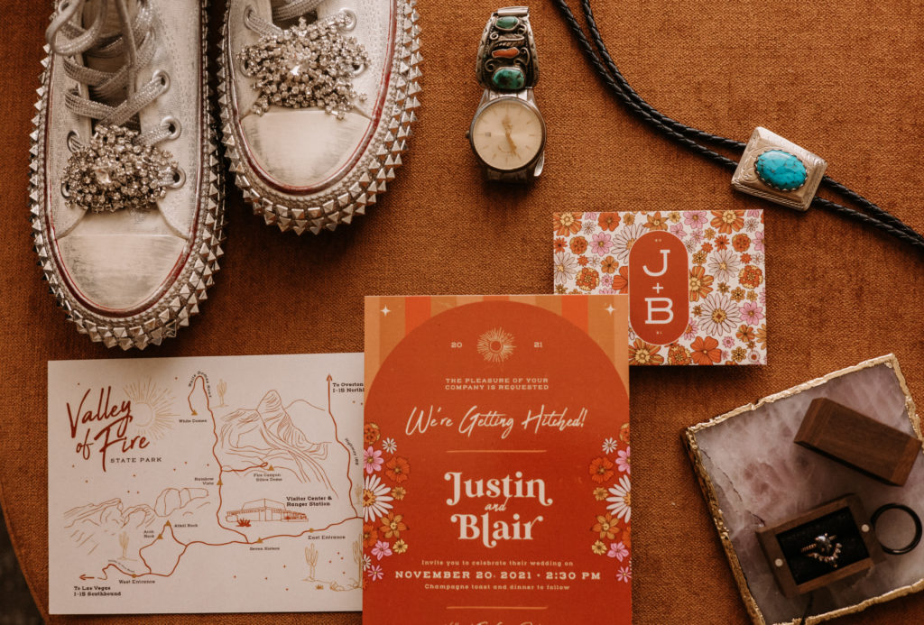 What is a boho styled wedding. Boho style stationary with a location card to valley of fire, couples invite in a burnt orange and wild flowers. Details of the grooms watch and turquoise bolo tie along with the brides custom converse wedding day shoes.  