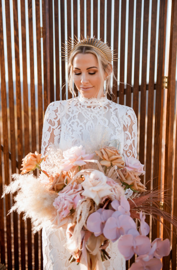 Boho bride with a gold metal boho crown. Wearing a long sleeve turtleneck white lace dress holding an assortment of boho style flowers for a bouquet. 