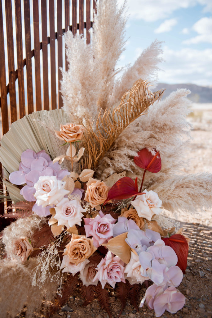 What is a boho styled wedding. Big lush roses mixed together with palm leaf, feathers and pampas for a boho style floral arrangement set up at the altar in Desert Love Land. 