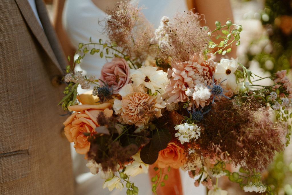 What is a Rustic & Whimsical Styled Wedding? A rustic and whimsical inspired bridal bouquet with blue thistle, seeded eucalyptus, roses, and dahlias. 
