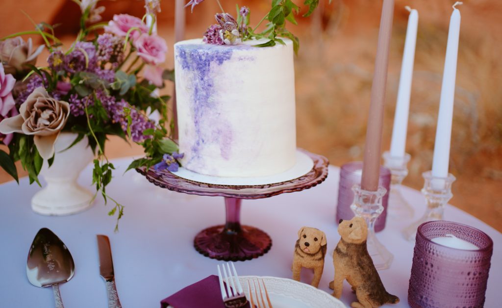 How To Include Your Dog on Your Wedding Day! Miniature dog cake toppers next to one tier white and purple wedding cake on dessert table. 
