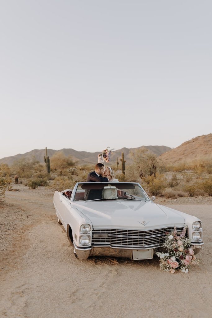 Newlyweds off in the middle of the desert in a vintage Cadillac car kissing 