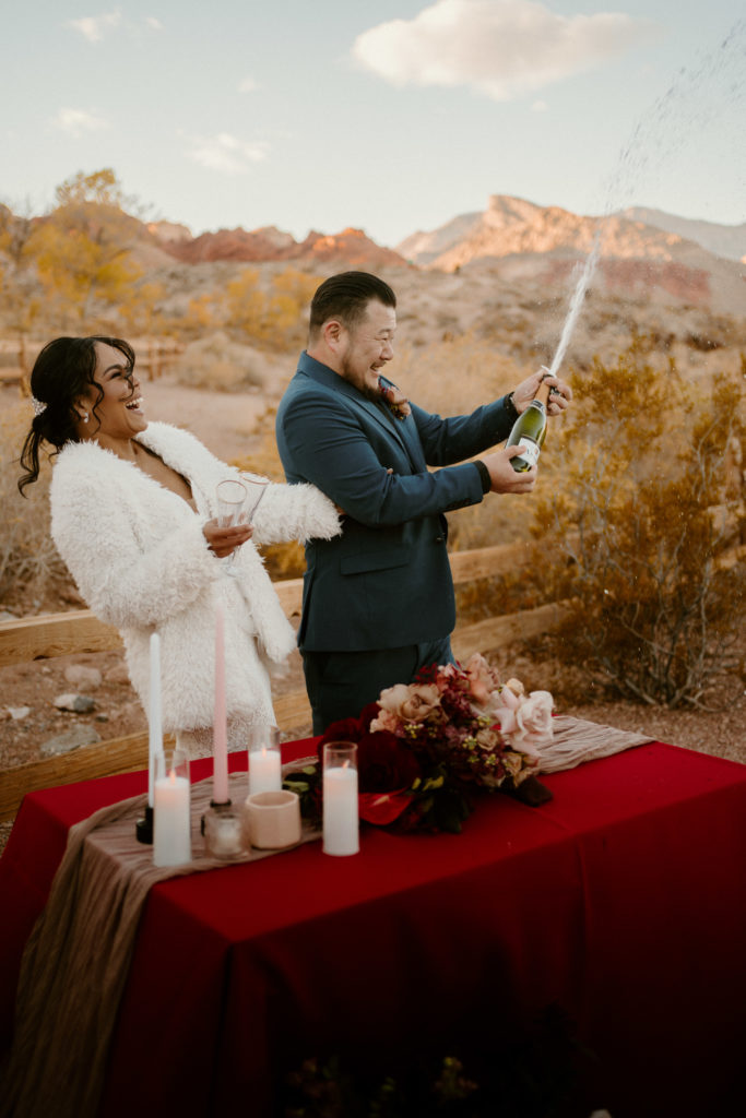 How to decide if you want an elopement or traditional wedding. Newlyweds pop champagne bottle at the cake table before cheering 