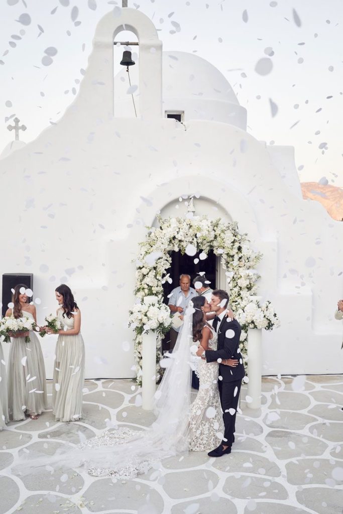 Newlyweds kissing at the altar in front of the greek church while flower pedals are being thrown