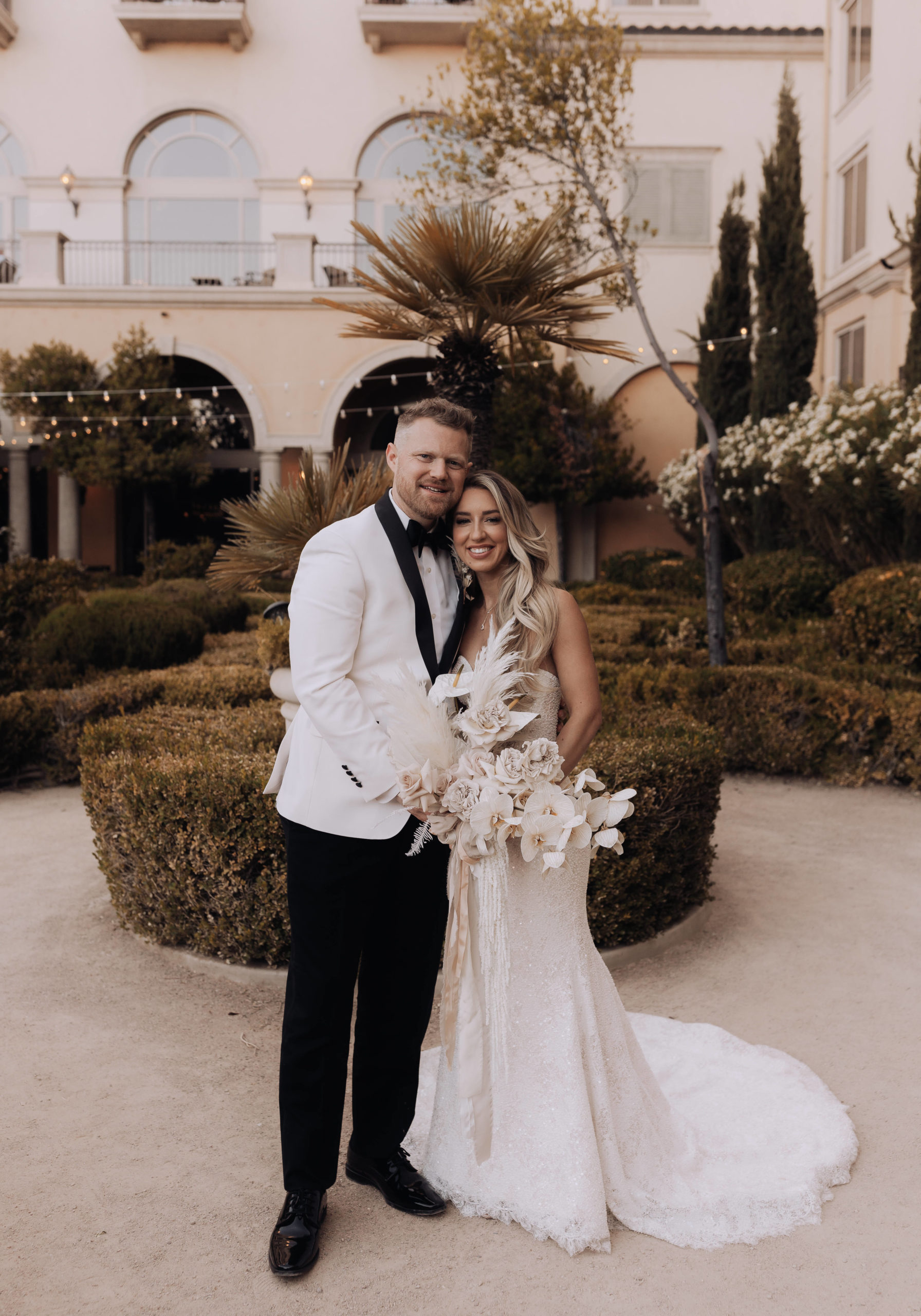 Lake Las Vegas Meets Modern Boho Bride. Newlyweds pose for a photo in the pathway of the beautiful shrubbery, white florals and bistro lighting before heading to reception 