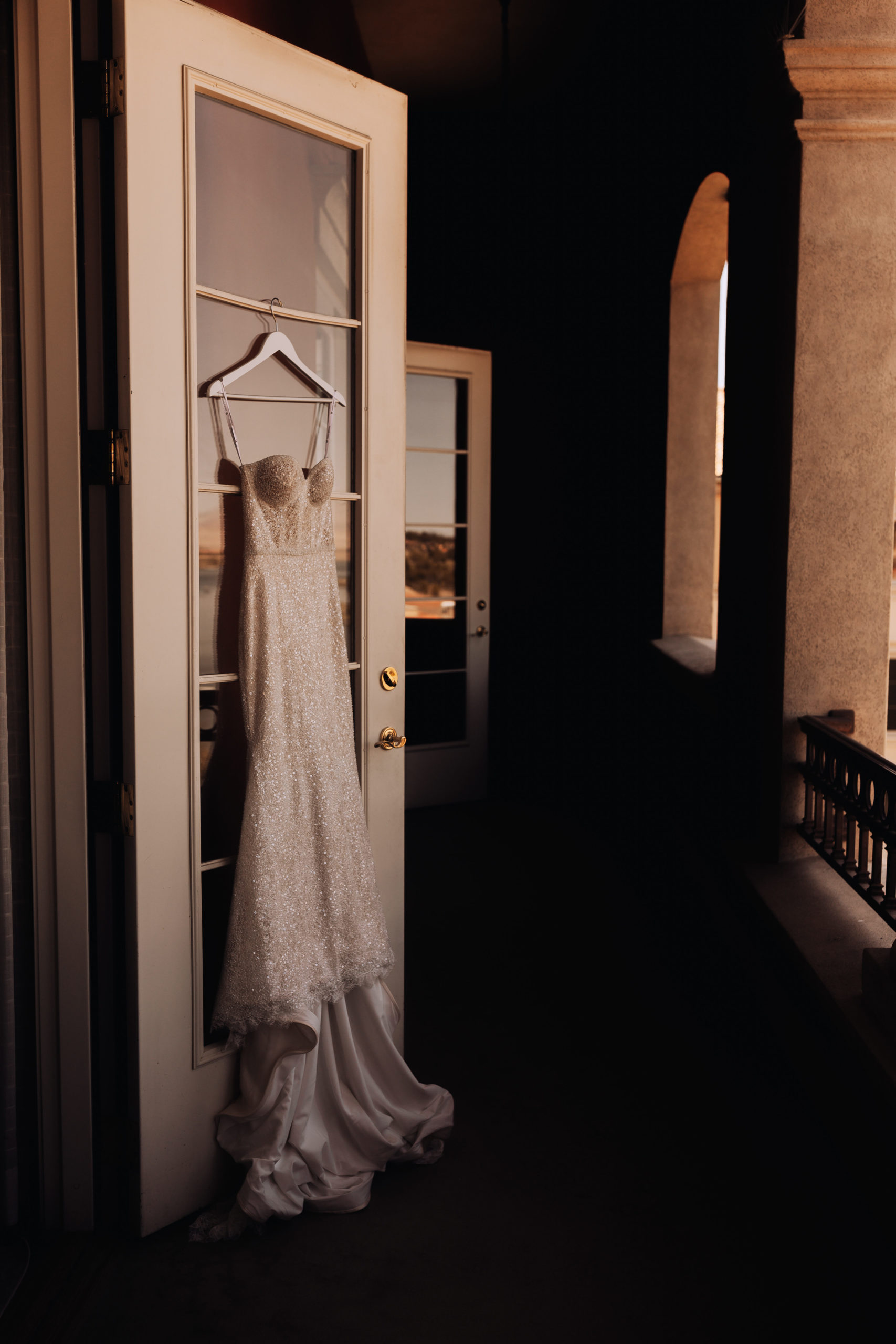 Lake Las Vegas Meets Modern Boho Bride. The brides beautiful lace corset wedding dress hanging on the glass door to the patio of the bridal suit
