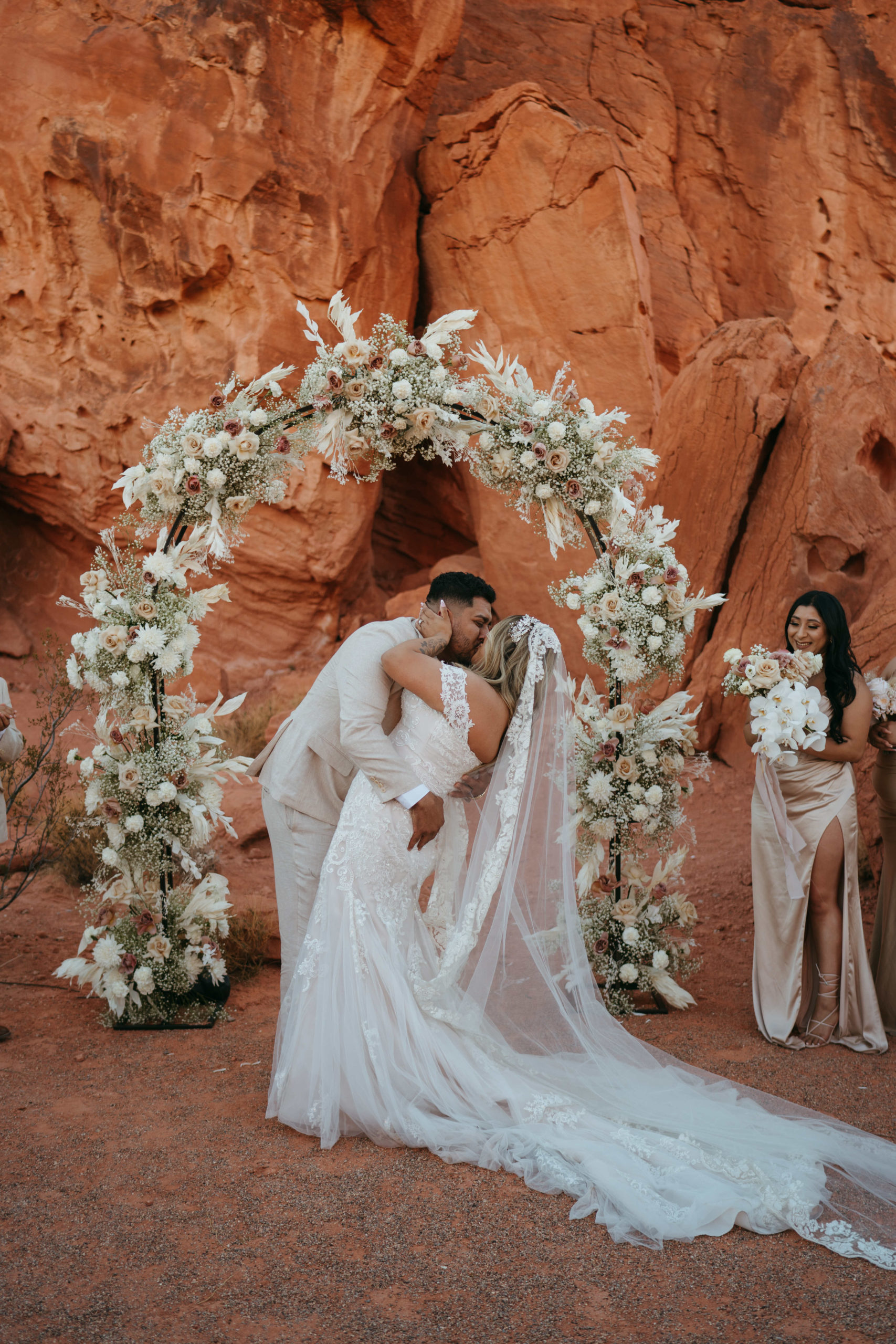 Modern Monochromatic Desert Micro-Wedding. The groom dips the bride at the floral arch altar for their first kiss as a married couple