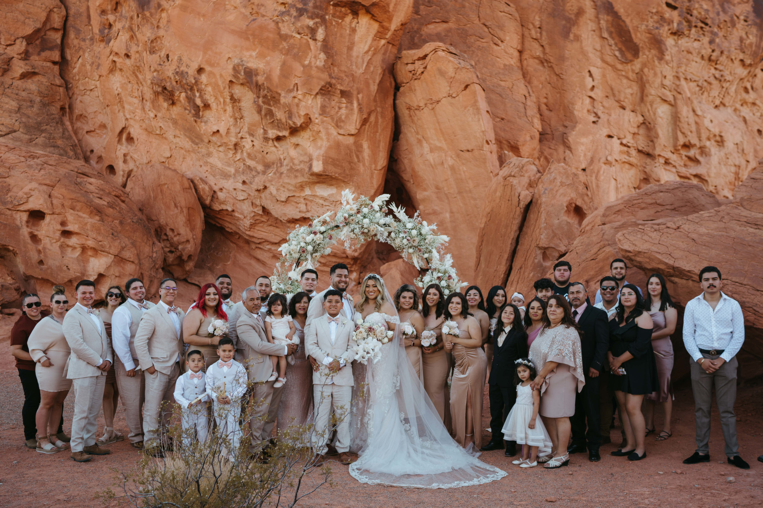 Modern Monochromatic Desert Micro-Wedding. Family and friends of the bride and groom all gather together in front of the floral arch to take a photo with the bride and groom