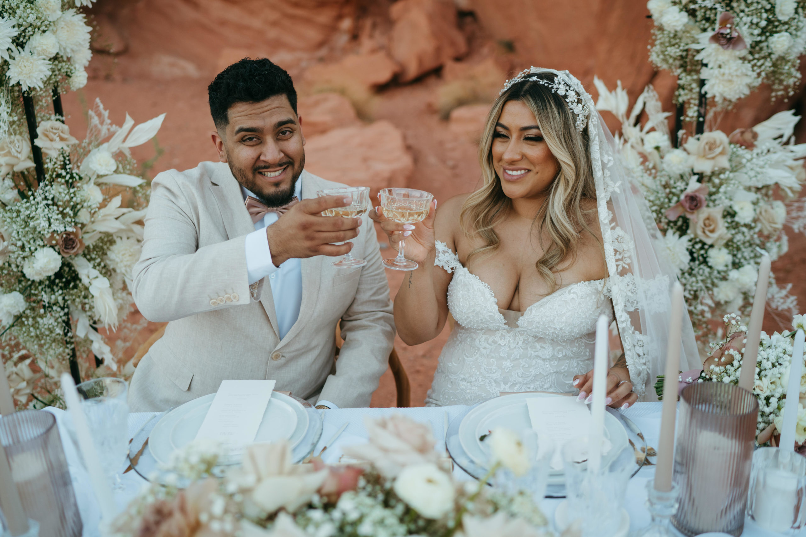 Modern Monochromatic Desert Micro-Wedding. The bride and groom cheers with champagne while they sit back and relax at the sweetheart table 