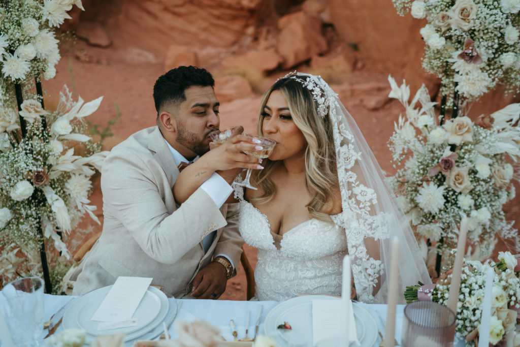 Modern Monochromatic Desert Micro-Wedding. Bride and groom drink champagne at the sweetheart table  