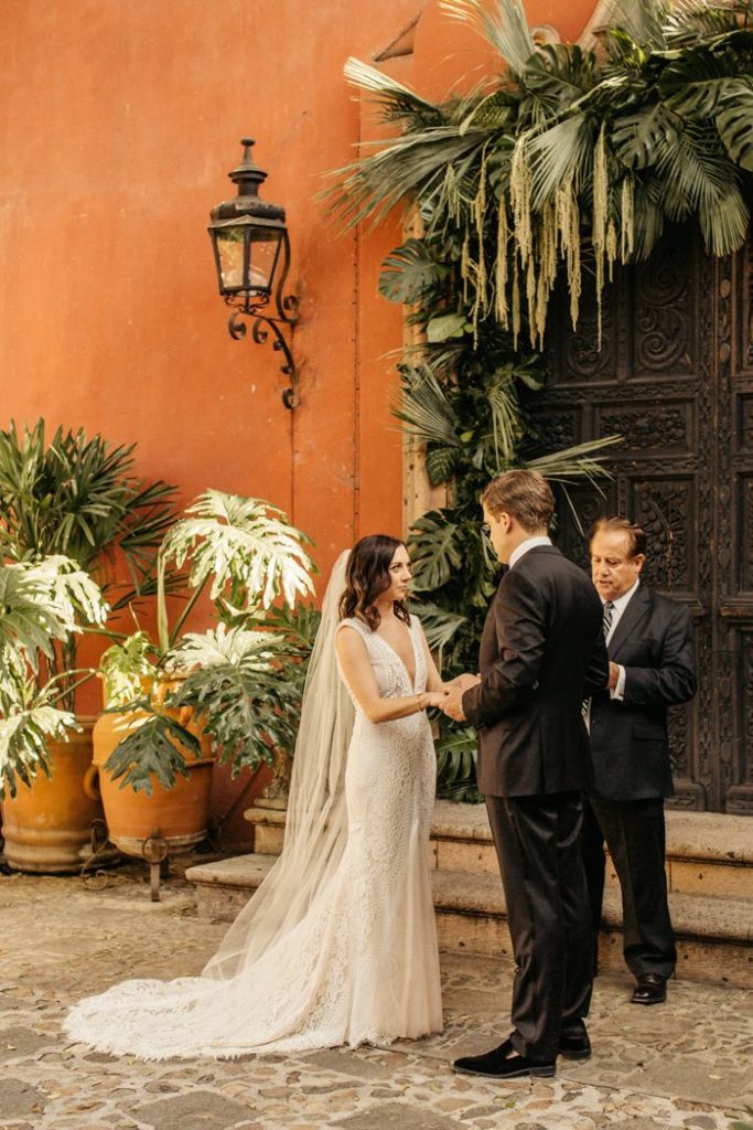 Bride and groom exchange vows in front of a colorful historic San Miguel building 