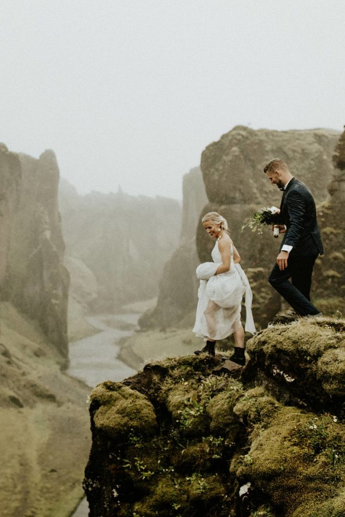 Bride and groom scaling the green hills of Iceland
