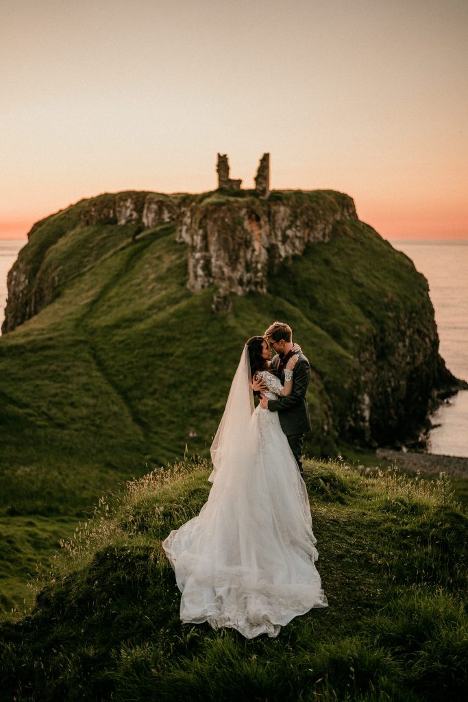Newlyweds kissing at the top of the cliff  of Dunluce Castle in Ireland