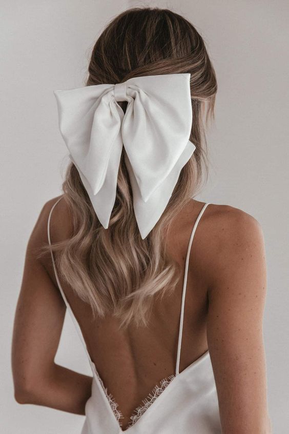 Half up hair pulled back with soft loose curls in a white silk bow 