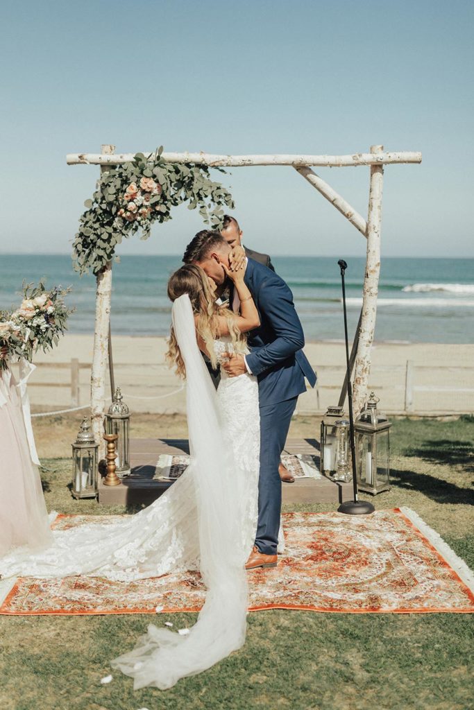 Top 10 Destination Wedding Locations for 2023! Newlyweds kissing at the altar at a beachfront wedding in Malibu.