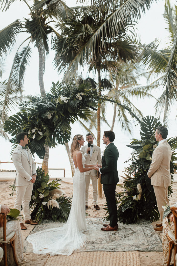 Bride and groom holding hands at the altar in front of a tropical circle arch in this Boho jungle wedding in tulum