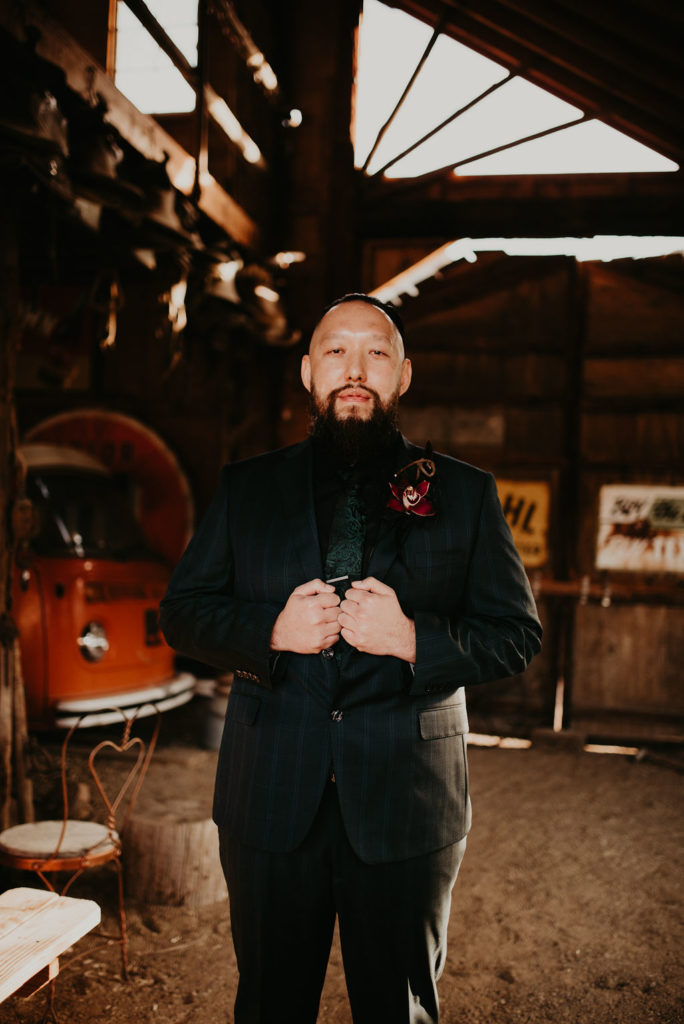 Groom in all black with moody red boutonniere