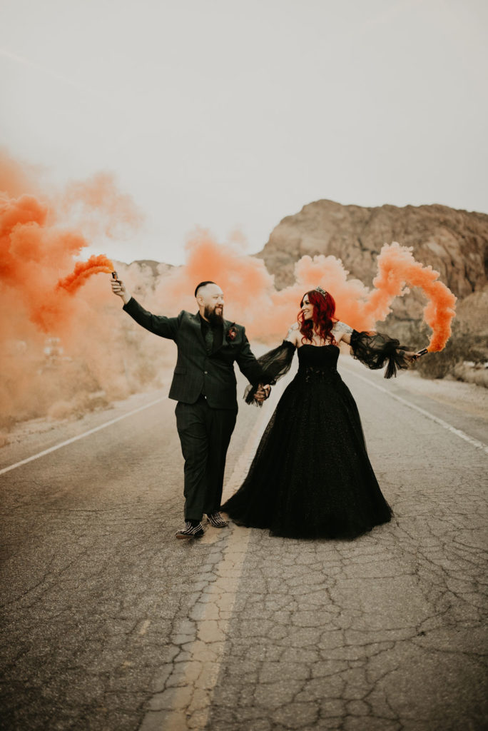 Newlyweds walking down road with orange smoke bombs for Halloween Elopement at Nelson's Ghost Town