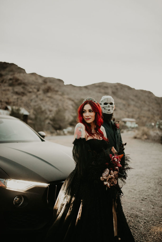 Groom in Mask next to Bride leaning on black car for Halloween Elopement at Nelson's Ghost Town