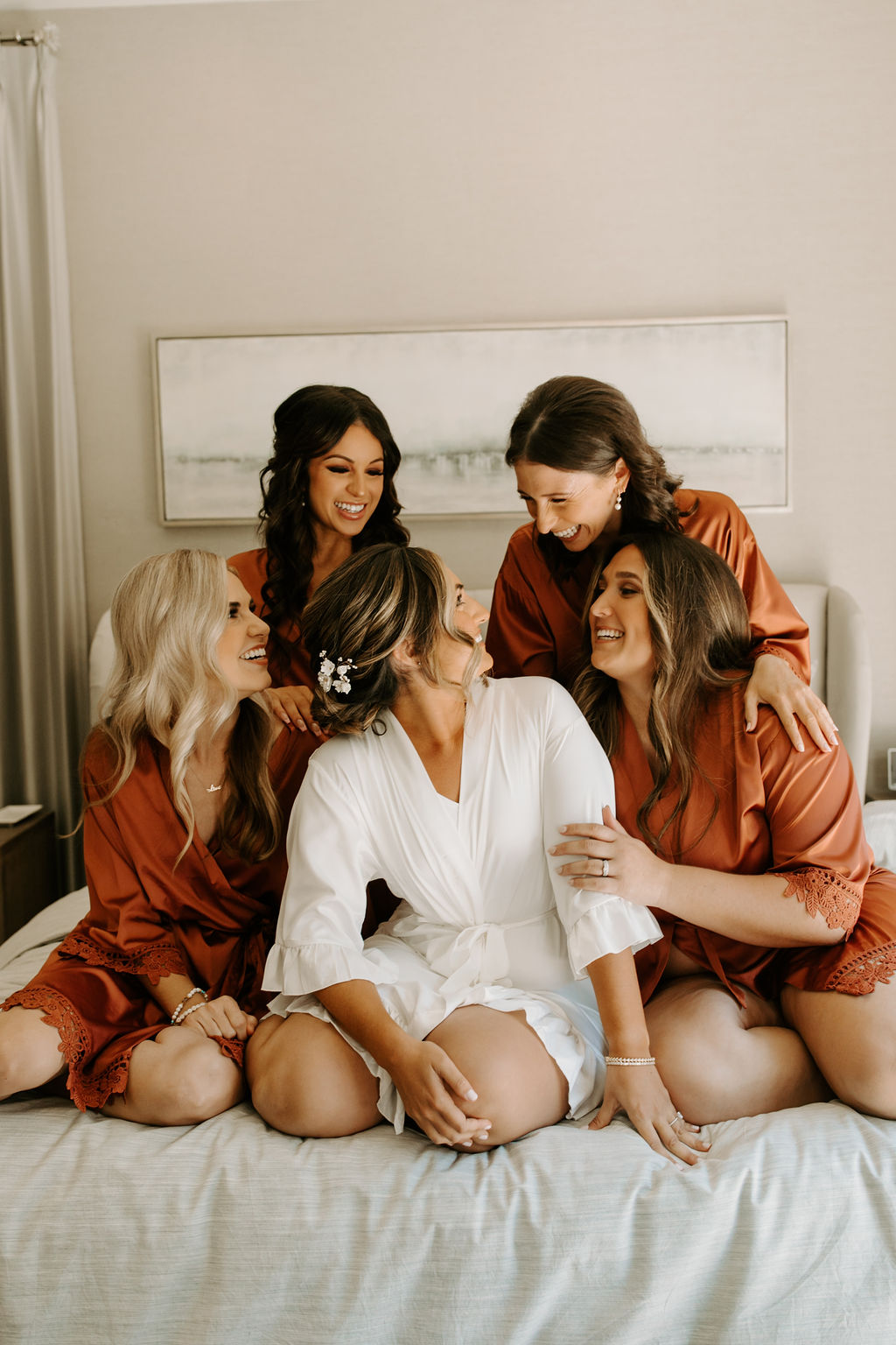 Brides in matching terracotta bridal robes getting ready with bride in white bridal robe 