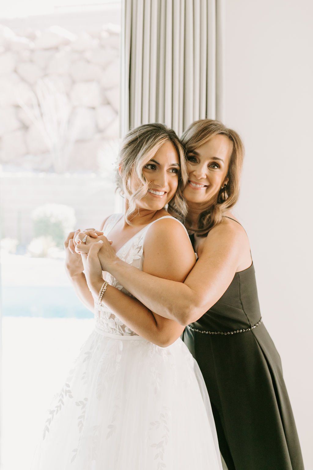 Bride smiling and hugging mother while getting ready 