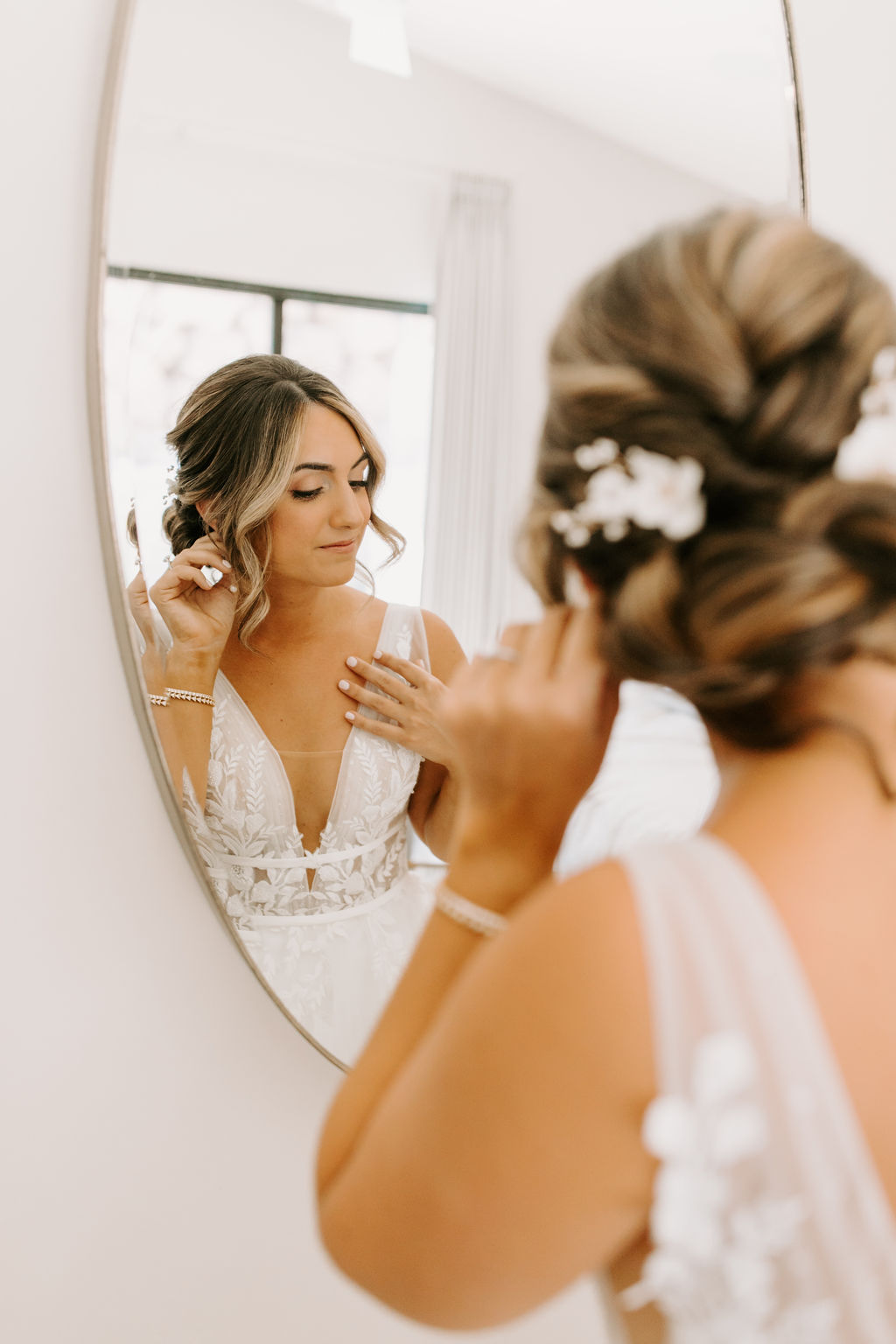 Bride putting earrings on in mirror 