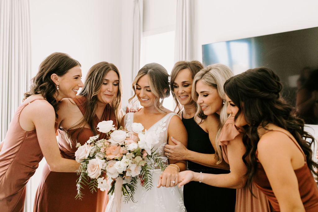Bridal party in mauve, dusty rose, dusty rust, and rust bridesmaid dresses admiring bouquet for Romantic Desert & Backyard Micro-Wedding